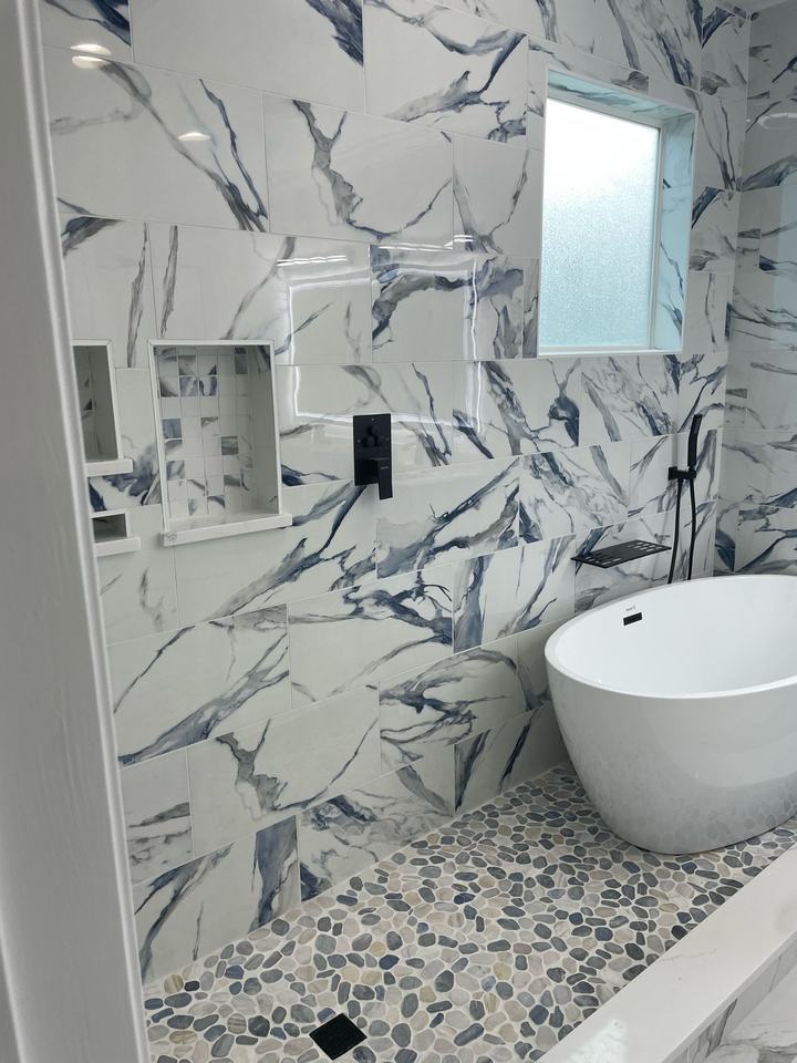 Blue-veined marble-look wet room with freestanding tub and pebble floor